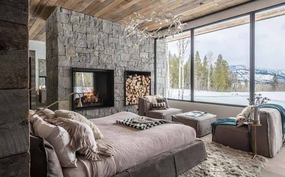 Montana bedroom with a stone fireplace looking out on a snowy mountain meadow